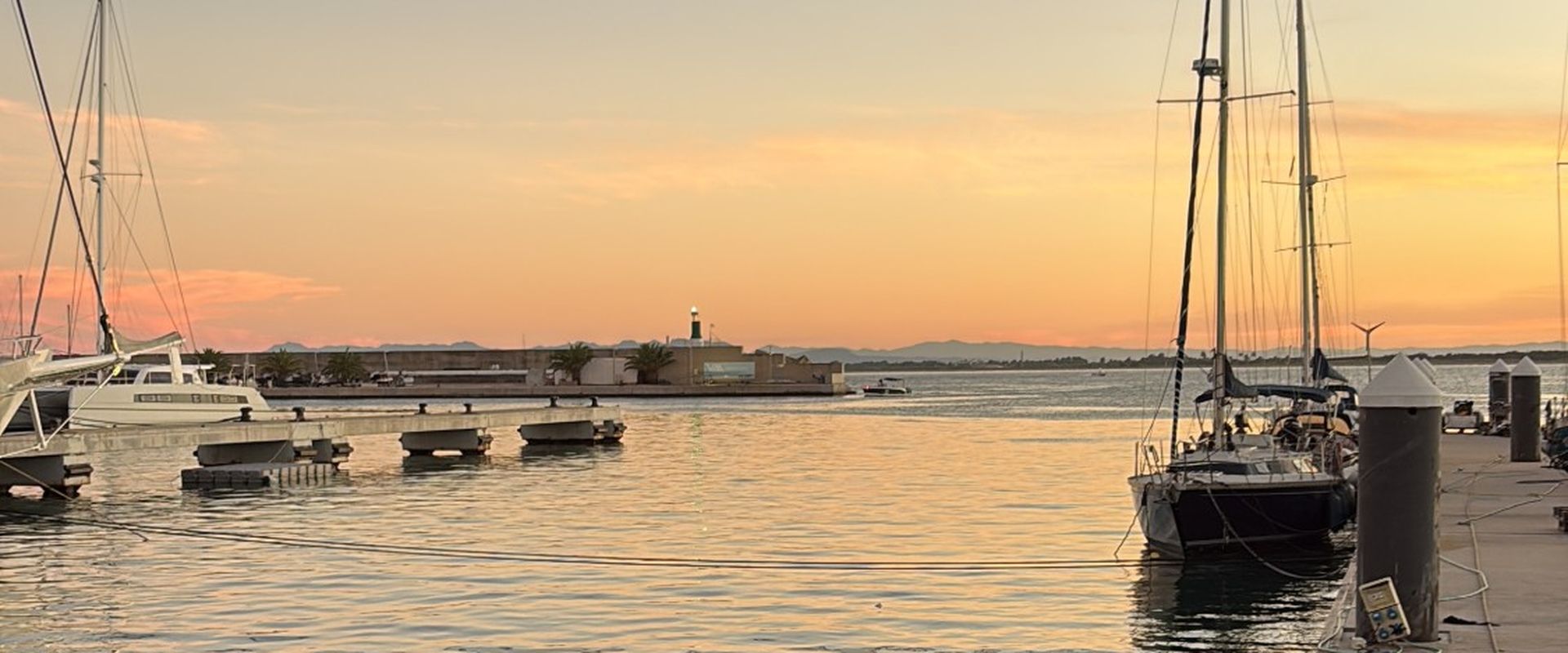 Atardecer en la bocana de un puerto deportivo, con veleros amarrados y la baliza verde encendida